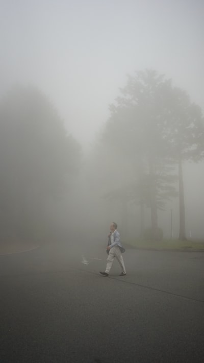 雾天，穿着白夹克和灰裤子的女人站在灰色的柏油路上